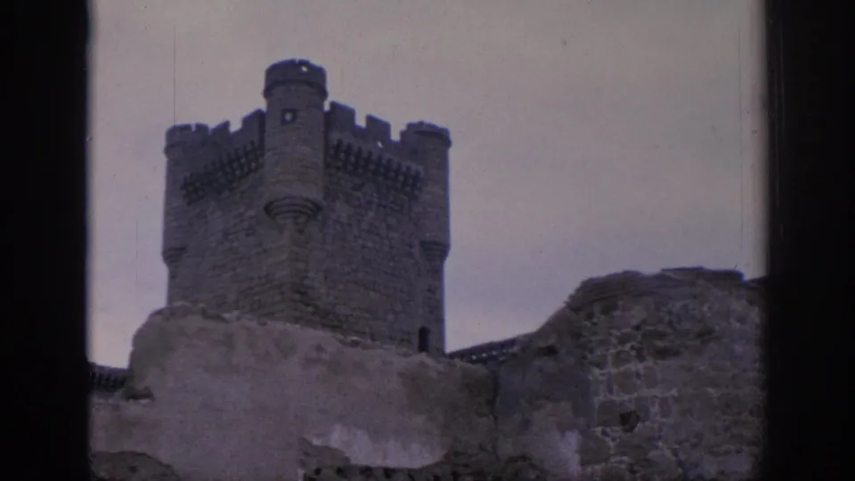 1966 Spain 8mm frame with a crenellated castle tower behind a broken stone wall, partly obscured by a dark window frame.