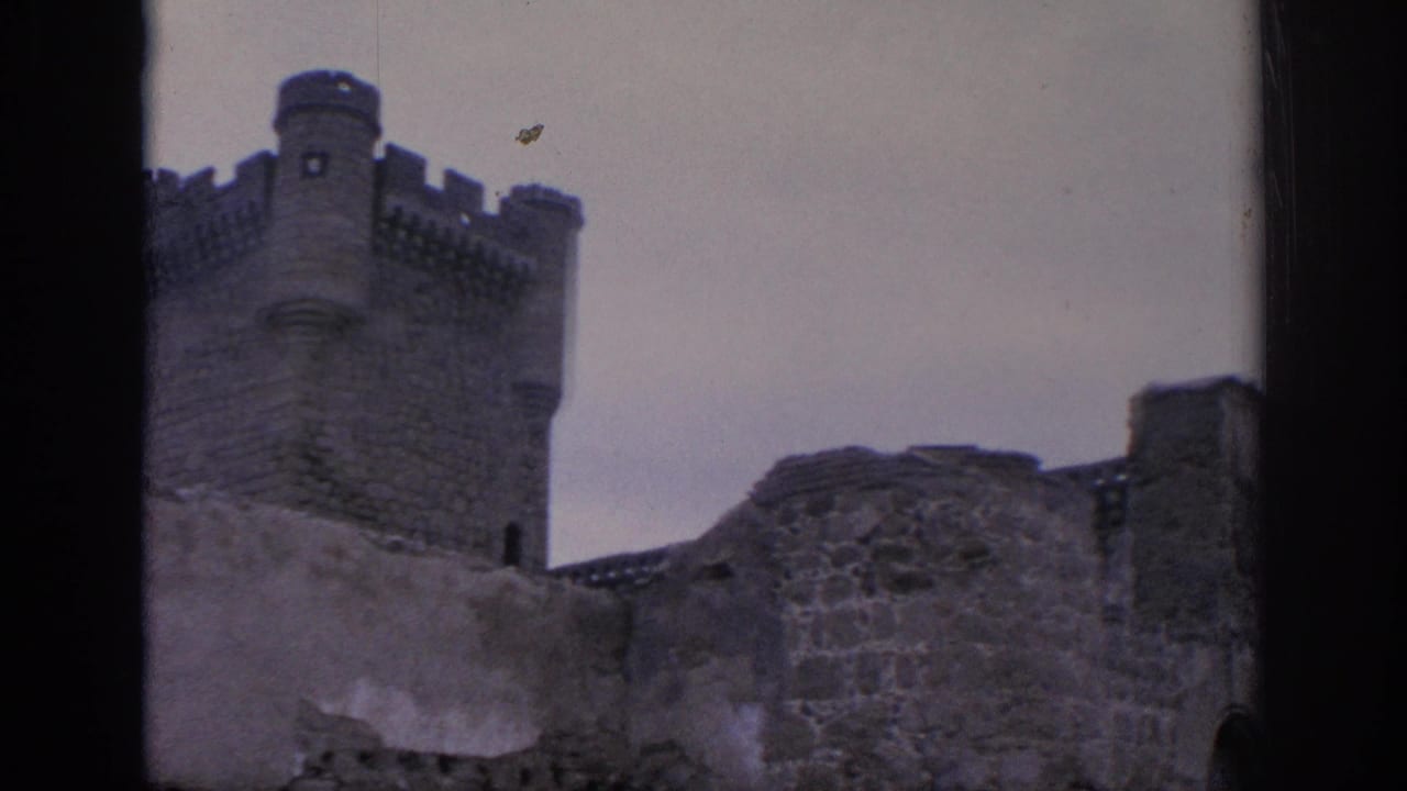 1966 Spain 8mm frame showing a castle tower, damaged stone wall, and open sky from a visitor viewpoint through a dark frame.
