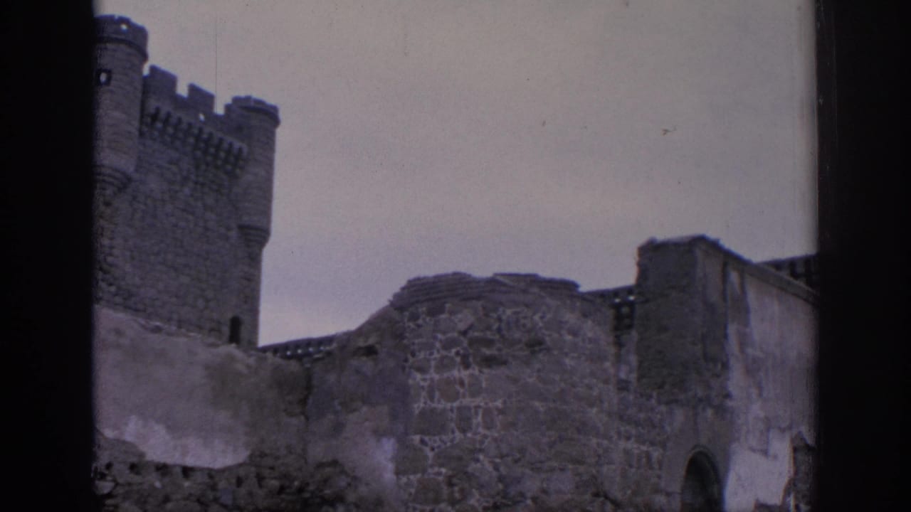 1966 Spain 8mm frame showing a crenellated tower, rough ruin wall, and arched opening under muted cloudy light.