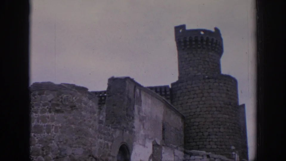 1966 Spain 8mm frame showing weathered stone ruins and a round crenellated tower beneath an overcast sky.