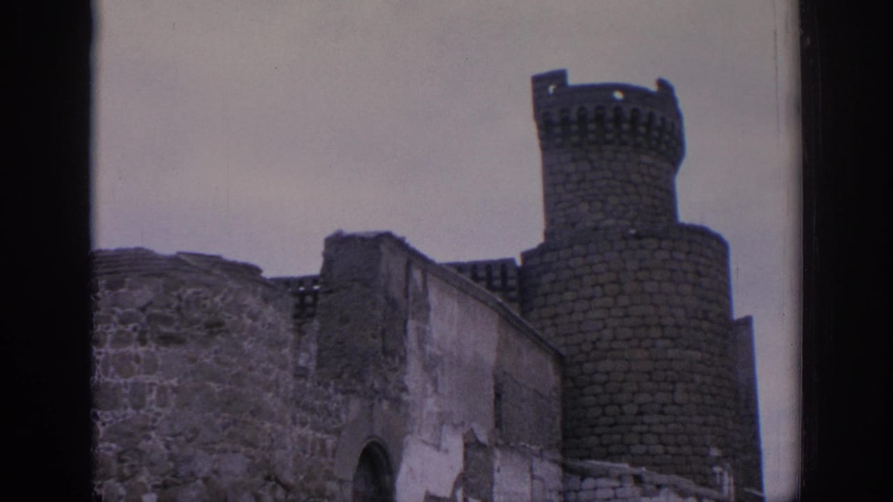 Crenellated round tower behind ruined stone and plaster walls.
