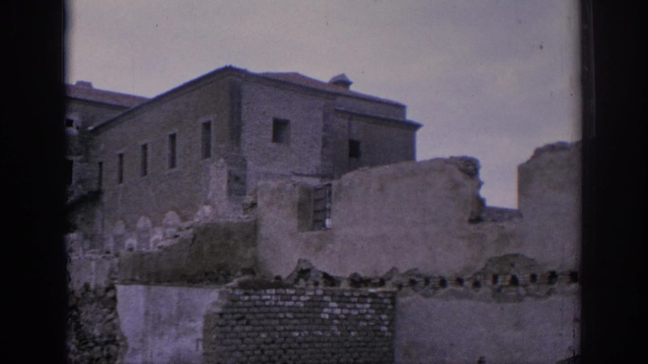 1966 Spain home-movie frame showing a large plain stone building behind broken walls and rough masonry.