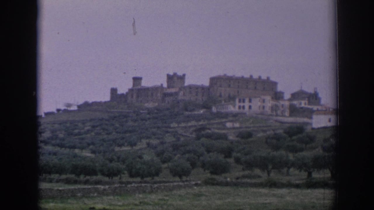Distant hilltop town above green terraced fields seen through a dark window frame.