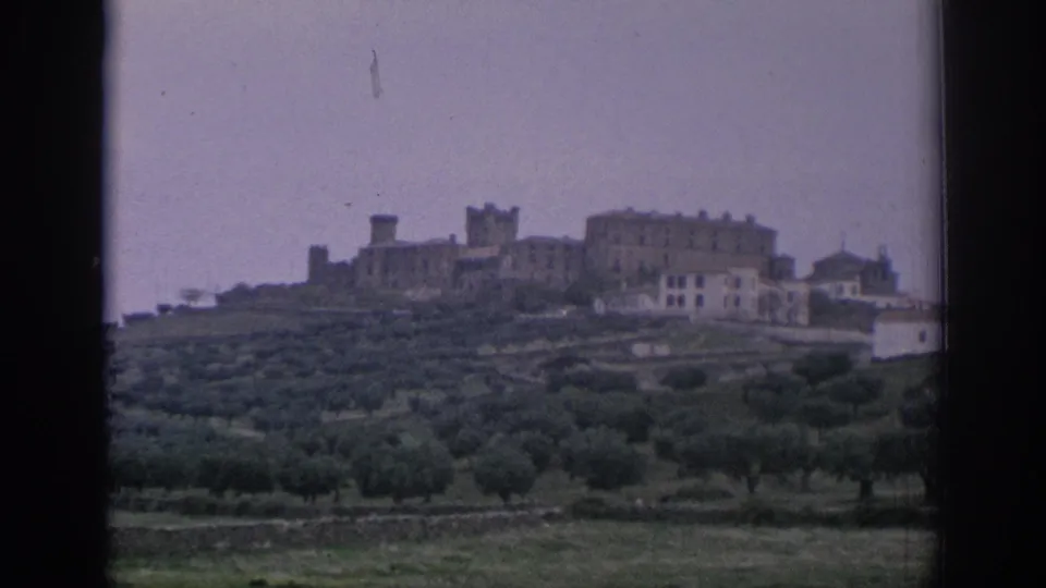 1966 Spain 8mm view of a hilltop stone town above verdant groves, partly framed by a dark window edge.