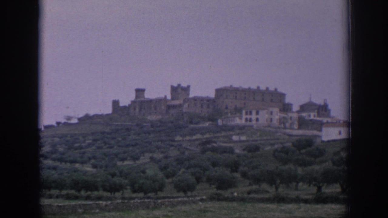 Distant Spanish hilltop architecture and cultivated green hills appear through the dark edges of the film or window frame.