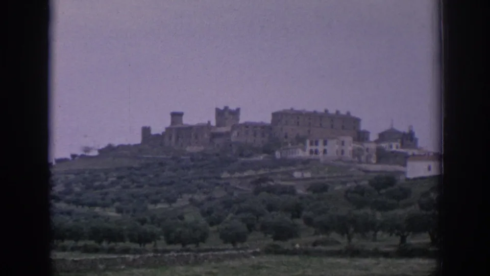 Distant Spanish hilltop architecture and cultivated green hills appear through the dark edges of the film or window frame.