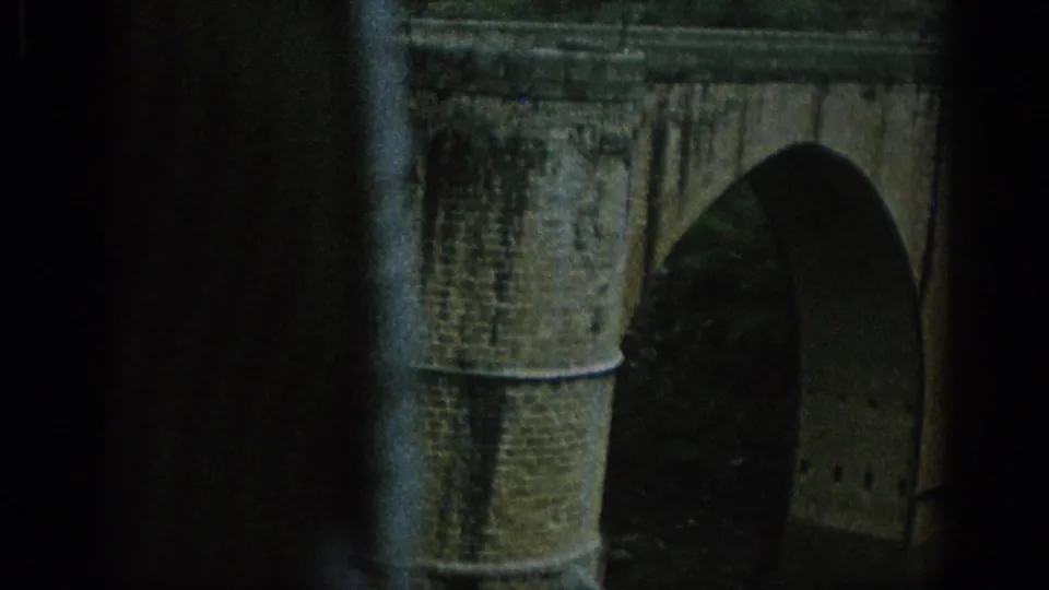 1966 Spain 8mm frame showing a masonry bridge arch in the foreground with a hilltop town and groves beyond.