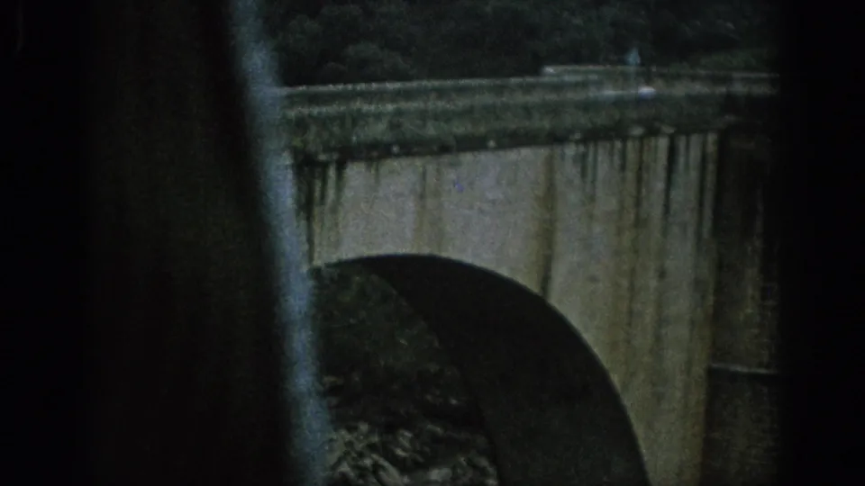 Masonry bridge arch and parapet fill the foreground, with dark frame borders and green landscape behind.