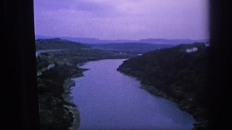 1966 Spain travel footage frame with a broad river curving between green valley slopes and distant hills.