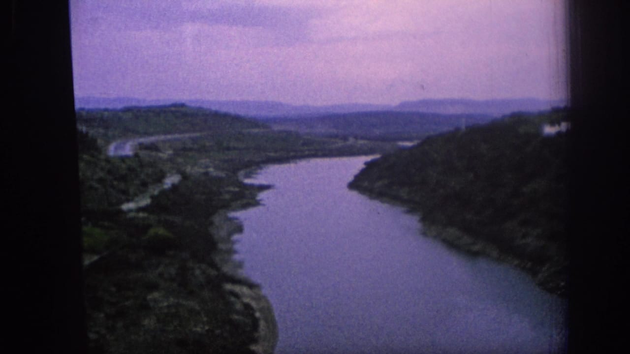 1966 Spain 8mm frame showing the river valley from above, with banks, fields, and distant ridgelines.