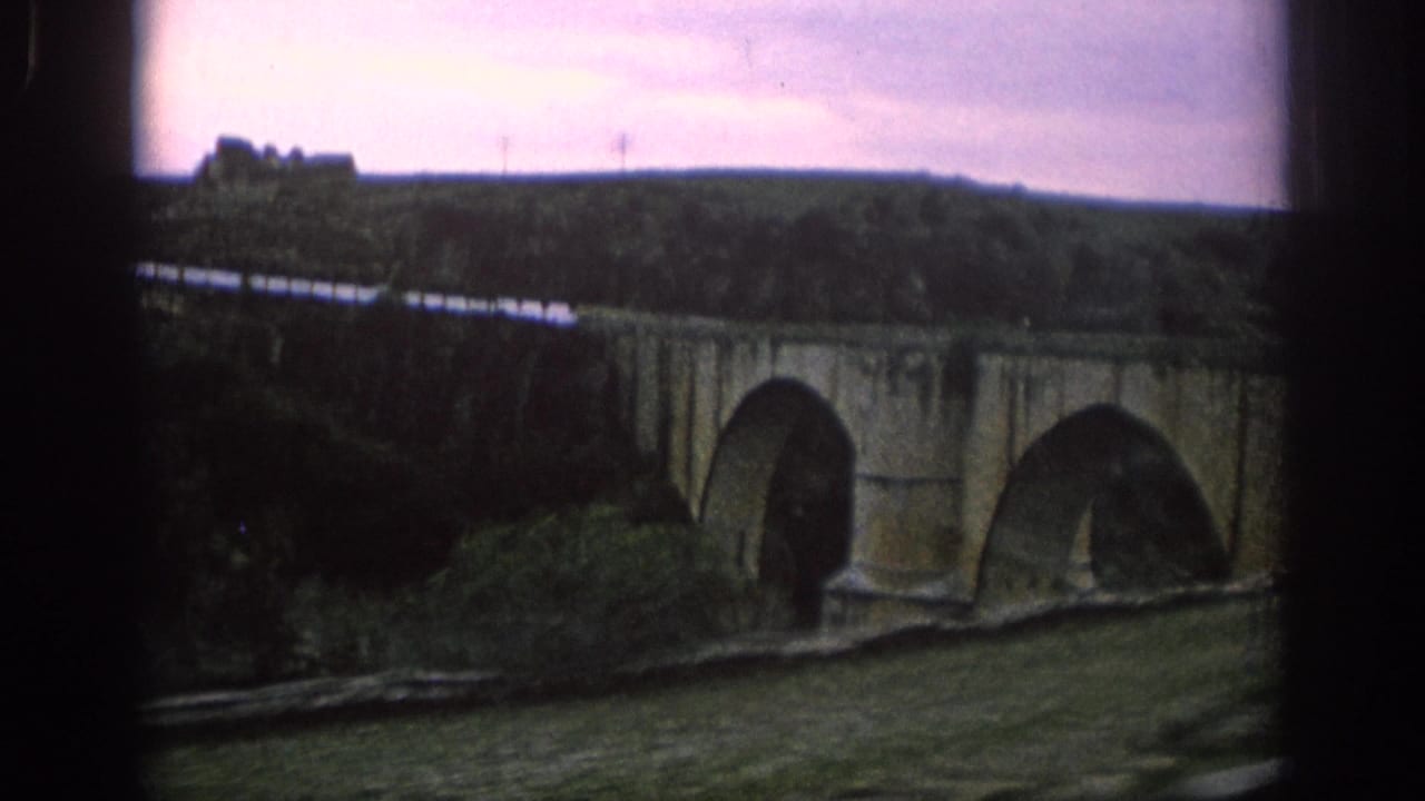 1966 Spain frame showing a train moving across a multi-arched railway bridge in a rural river valley.