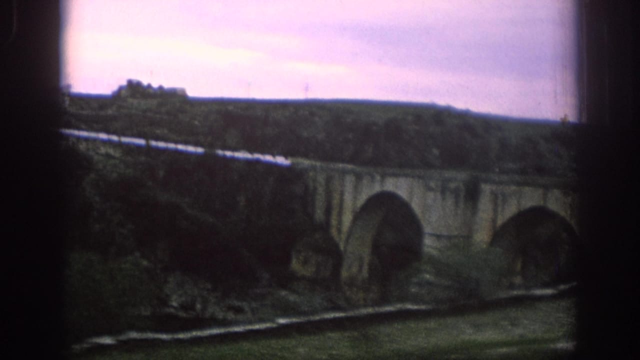 Stone arch bridge and rail line viewed through dark train window edges.