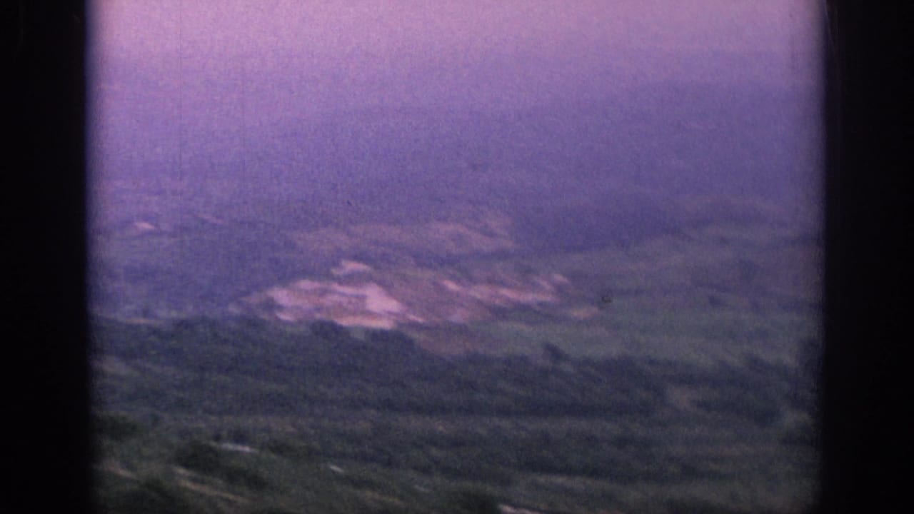 1966 Spain 8mm view across soft-focus rural hills and fields, with pale buildings faintly visible in the distance.