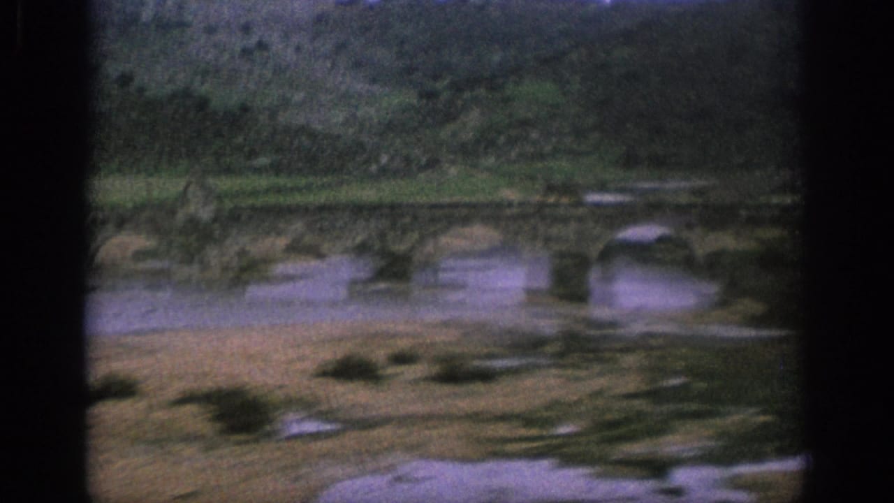 Stone arch bridge crossing a river below green hills.