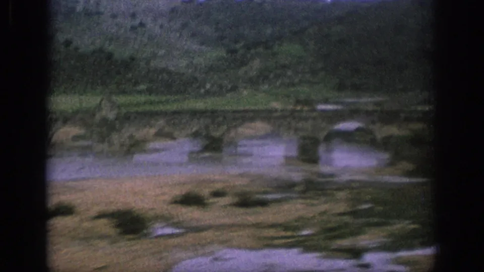 Aerial 8mm view of a historic-looking stone arch bridge spanning a river in rural Spain.
