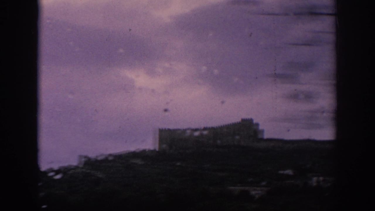 Dark train-window border with a distant stone structure silhouetted on a ridge.