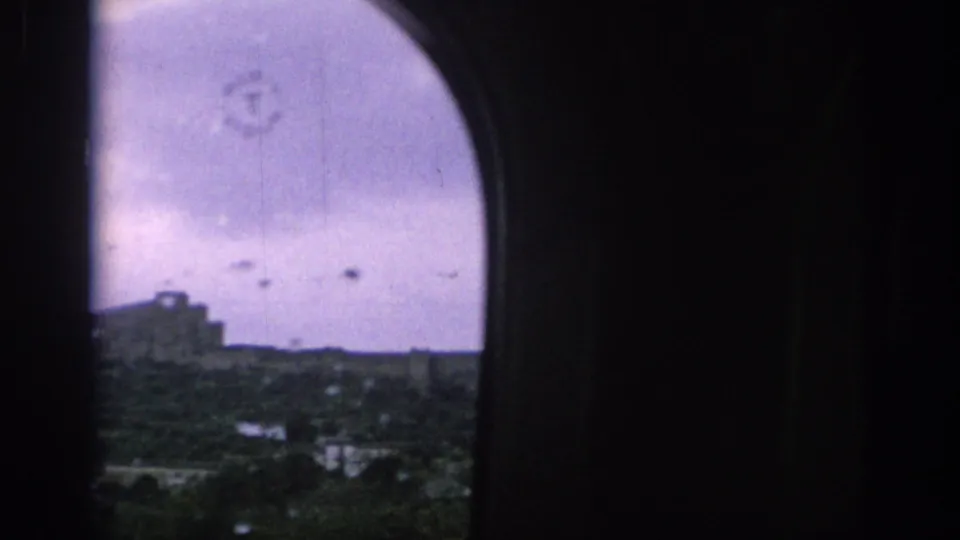A cropped 1966 Spain travel view from a train window, with dark interior framing, wet glass, cloudy sky, and a distant structure on the hillside.