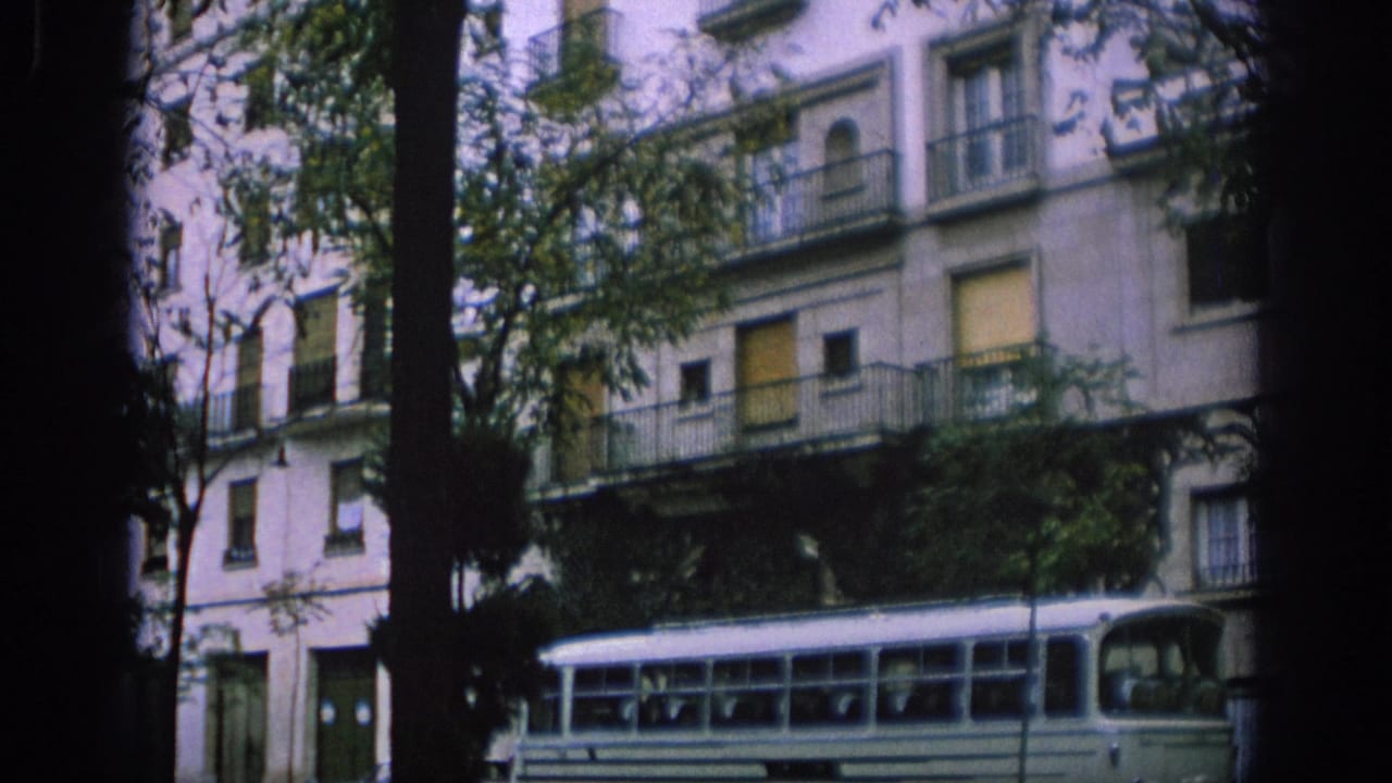 White bus passes trees and a multi-story apartment building with balconies.
