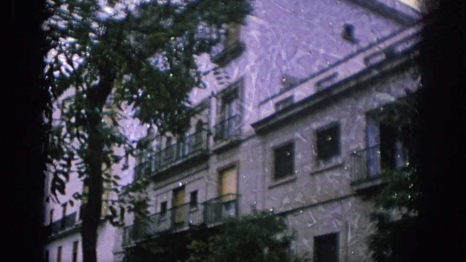 1966 Spain home-movie view of an apartment building with balconies and trees, seen from a moving or obstructed viewpoint.