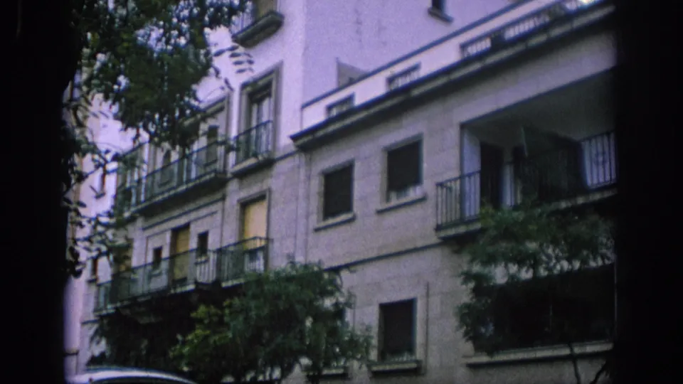 1966 Spain street-level view of a tall apartment building with balconies, shuttered windows, and leafy trees in front.