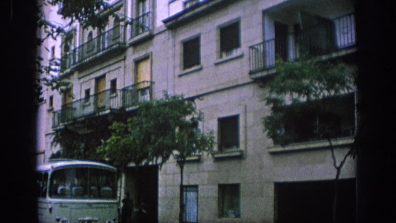 Apartment facade with balconies, open windows, trees, and a bus partly visible below.