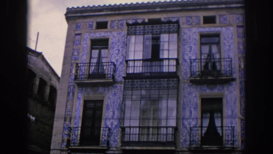 1966 Spain home-movie view of a blue tiled building front with balconies, large glazed windows, and adjacent narrow street walls.