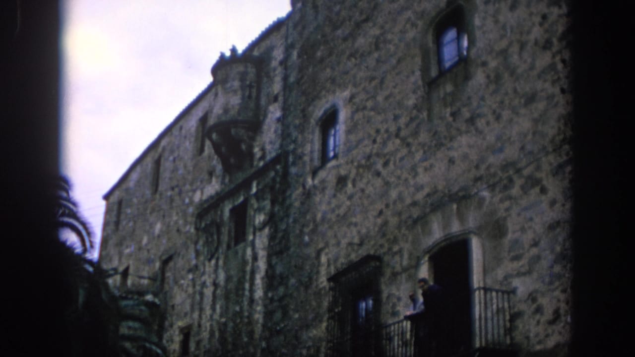 Low-angle view of a weathered stone building with small windows and an iron balcony.