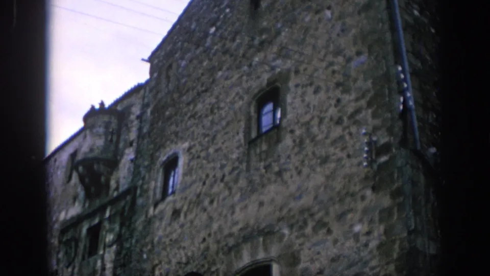 1966 Spain frame showing the textured stone wall of an older building with small windows, balcony detail, and cropped doorway area.