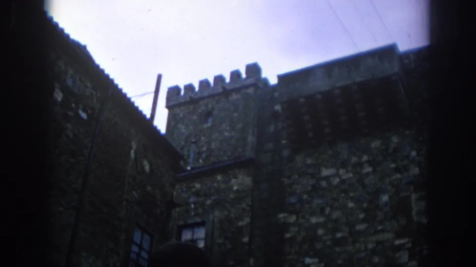1966 Spain 8mm frame with a low view of weathered masonry, battlements, a small window, and the shadowed side of the alley.
