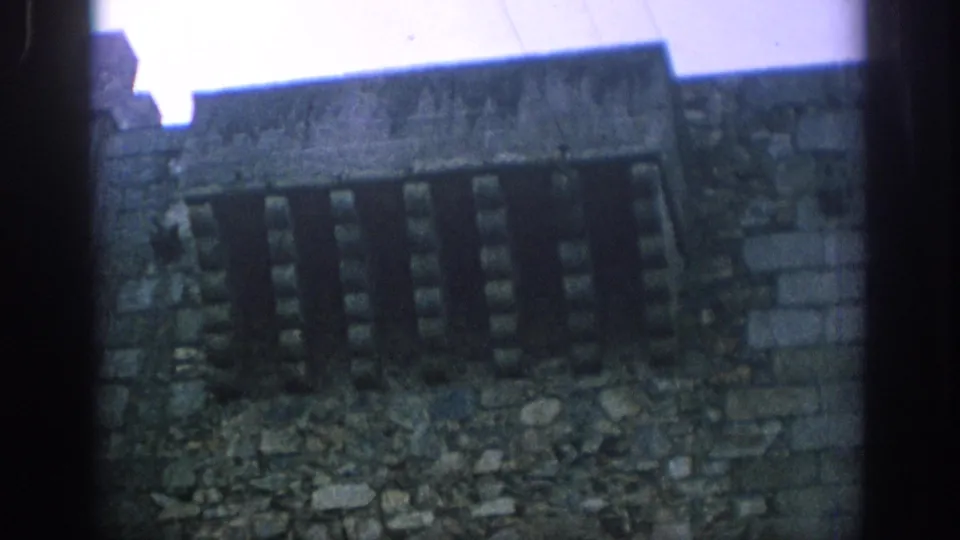 1966 Spain 8mm frame showing a closer view of rough stone masonry, blocked or shuttered windows, and uneven dark borders from the scan.
