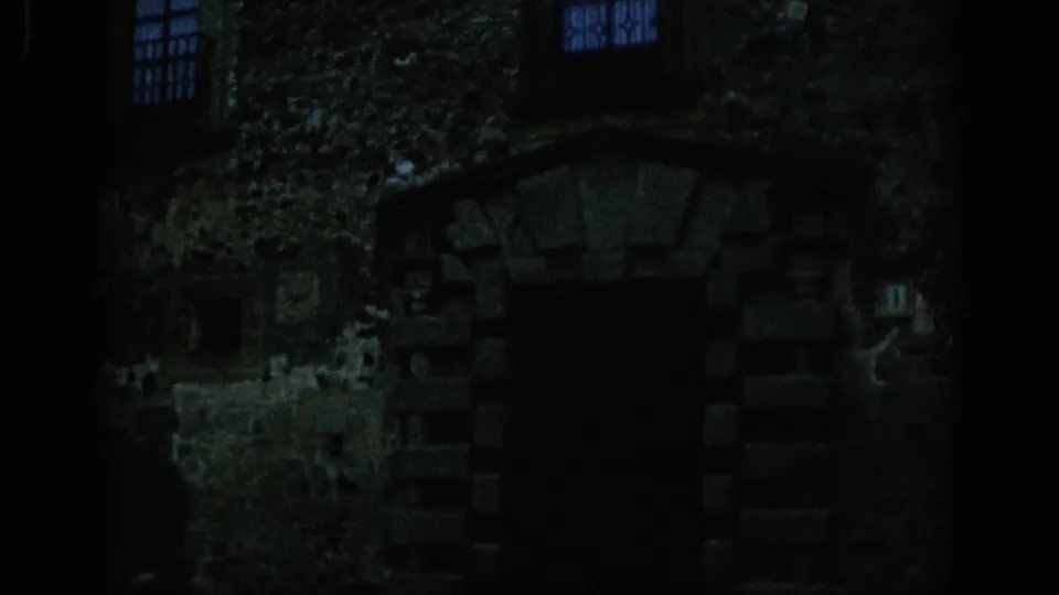 1966 Spain 8mm view of a dark castle doorway, uneven stone blocks, and small blue-tinted windows in low light.