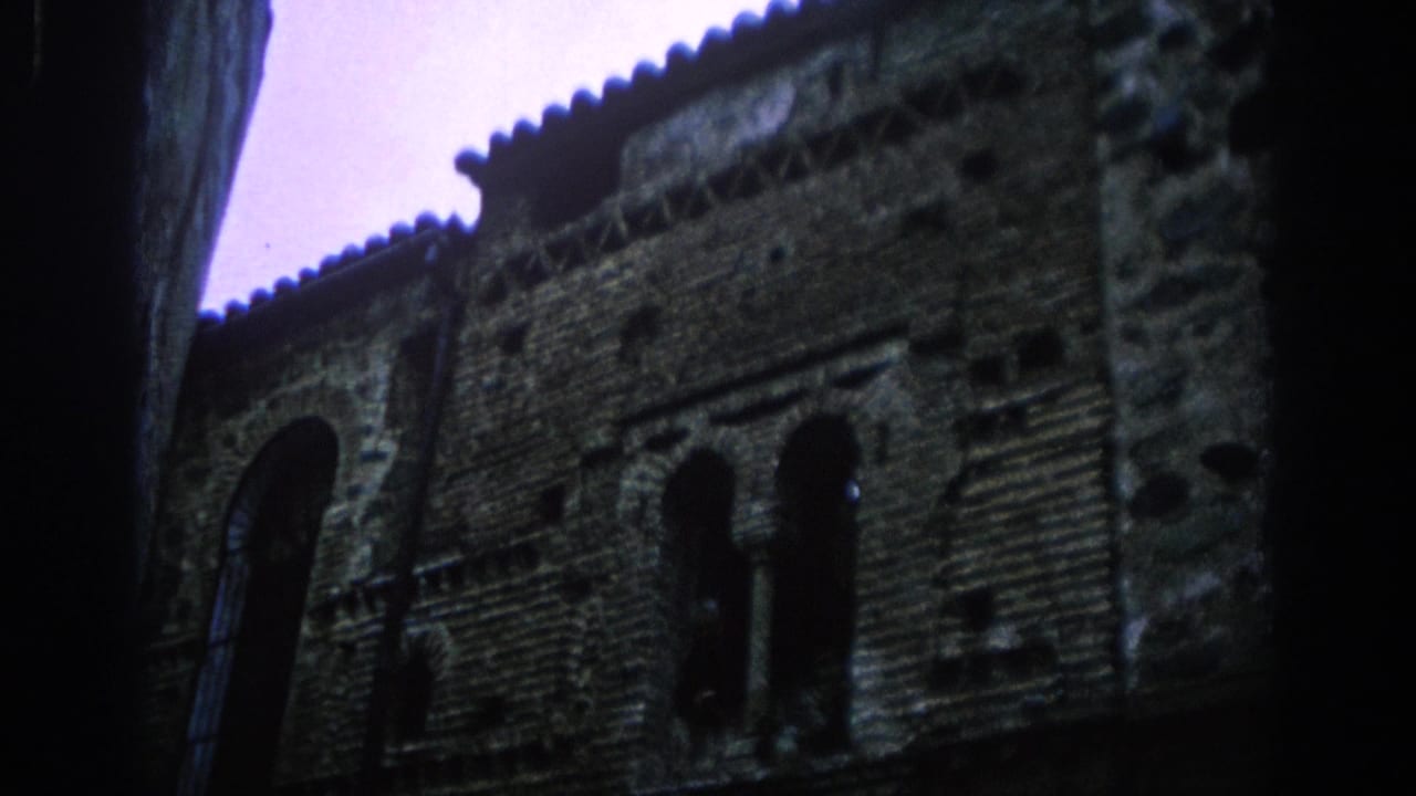 Dark brick building facade with arched windows and tiled roof edge seen from below.