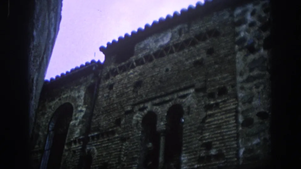 1966 Spain 8mm frame with soft focus on an older brick facade, arched windows, decorative masonry and a narrow strip of sky.