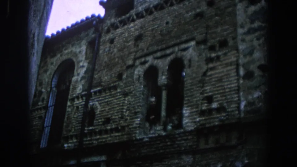 1966 Spain frame showing a closer angled view of the brick facade, paired arched windows, patterned masonry and low-light street framing.