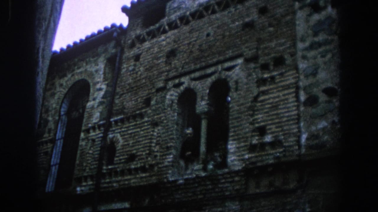 Low-angle view of a dark stone and brick facade with arched windows beneath a pale sky.