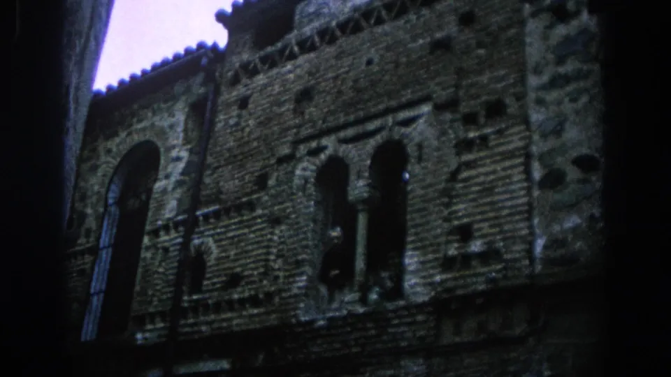 1966 Spain 8mm frame showing a weathered historic facade with arched windows, brickwork, and dark passage edges.