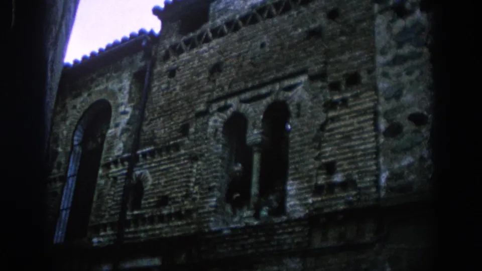1966 Spain 8mm still of a historic building facade, showing a tall arched window and textured masonry from below.