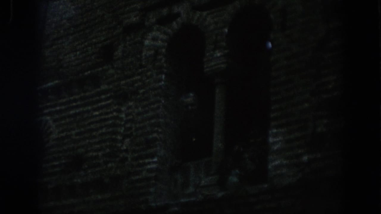 Dark 1966 Spain 8mm frame showing a masonry tower or wall with arched openings barely visible in low light.
