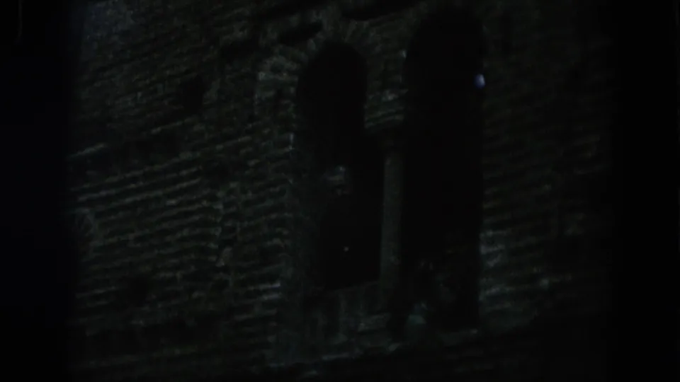 Dark 1966 Spain 8mm frame showing a masonry tower or wall with arched openings barely visible in low light.