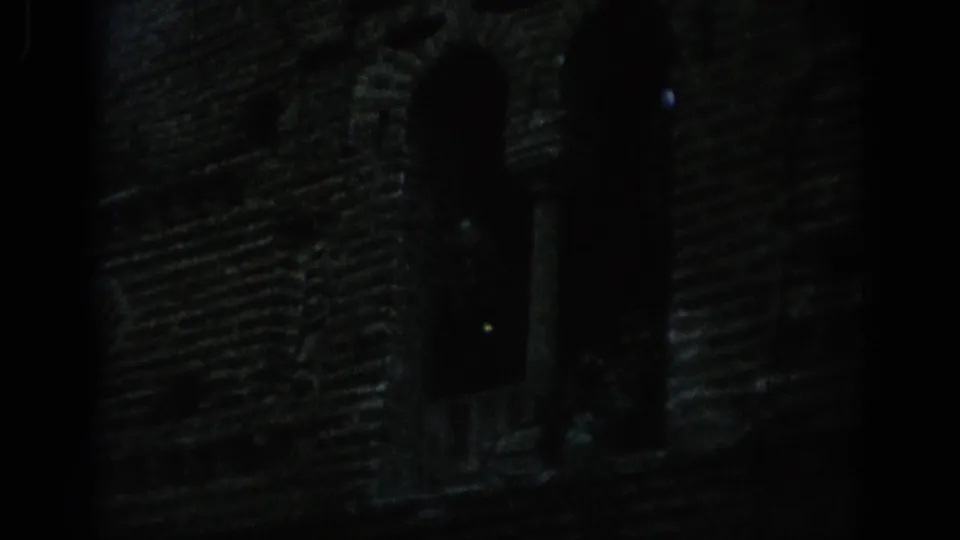 Underexposed 1966 Spain frame with a dark masonry facade, a tall arched opening and visible film edge.