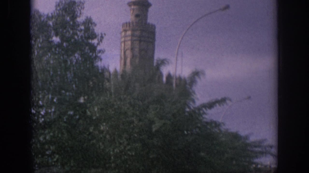 Stone tower partly hidden by leafy trees along a street.