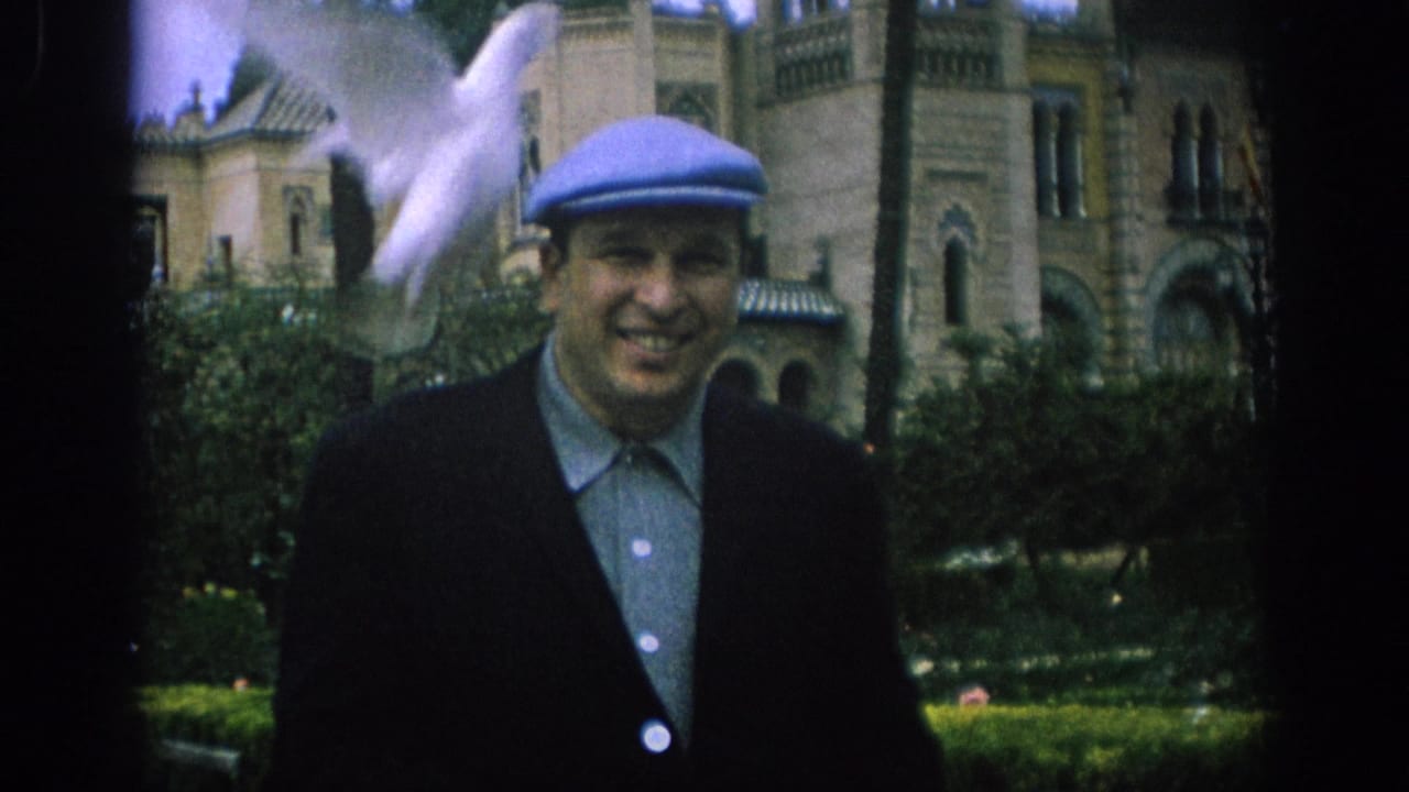 In Spain 1966, a smiling man in a blue cap stands in a garden as a white dove moves near his shoulder before an ornate stone building.