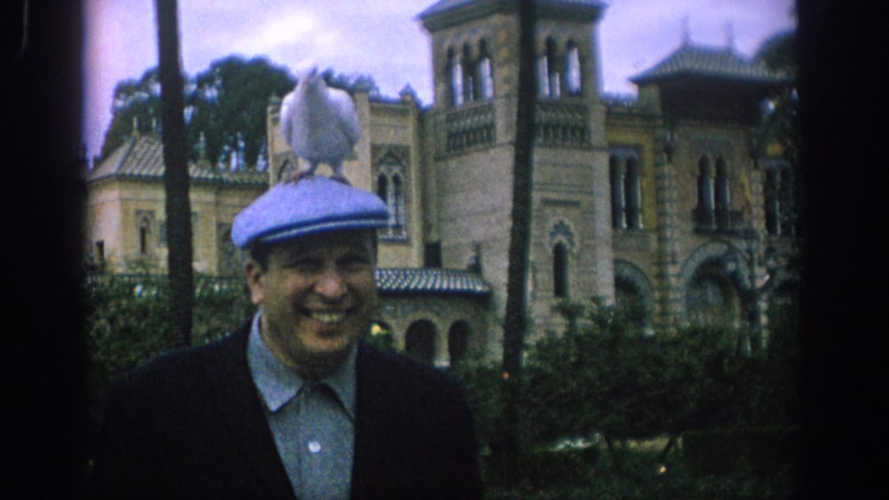 White dove perched on the top of a smiling man’s blue cap in a garden setting.