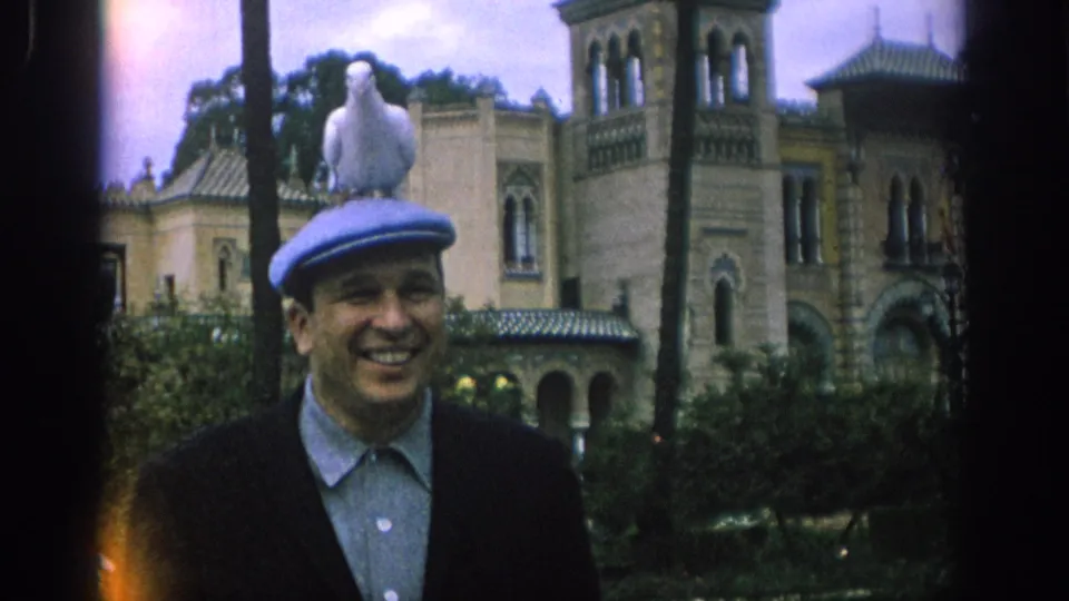 In Spain 1966, the man grins while the white dove remains perched on his cap in a landscaped garden before an ornate stone facade.