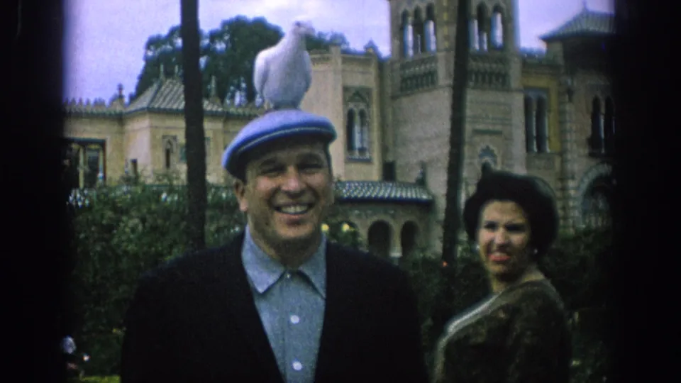In Spain 1966, a smiling woman stands beside the man while a white dove perches on his blue cap in the garden.
