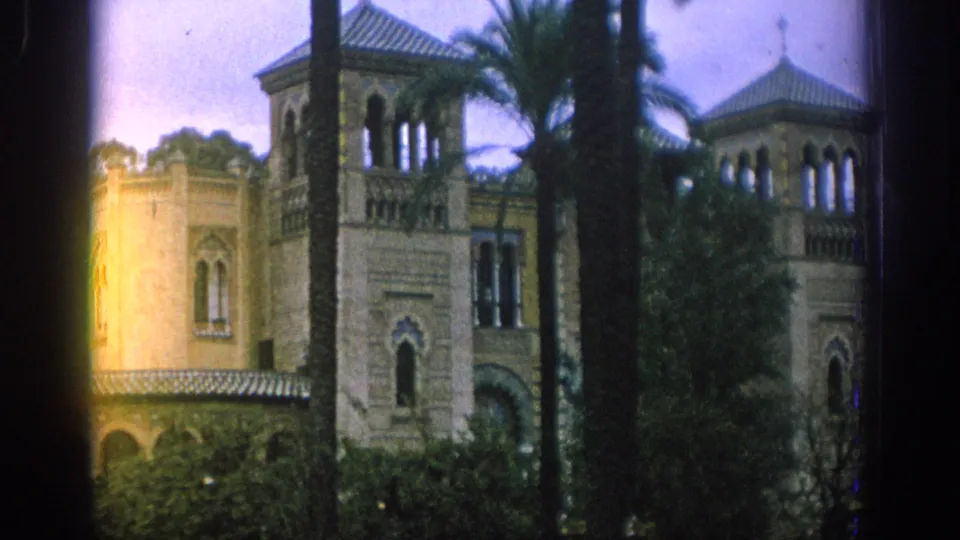 1966 Spain travel frame showing a Moorish-style facade with arched openings, palm trees, shrubs, and warm flare along the left side.