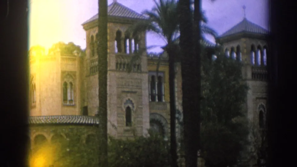 1966 Spain 8mm frame of a tan Moorish-style building with towers and palms, softened by yellow edge flare and handheld exposure variation.