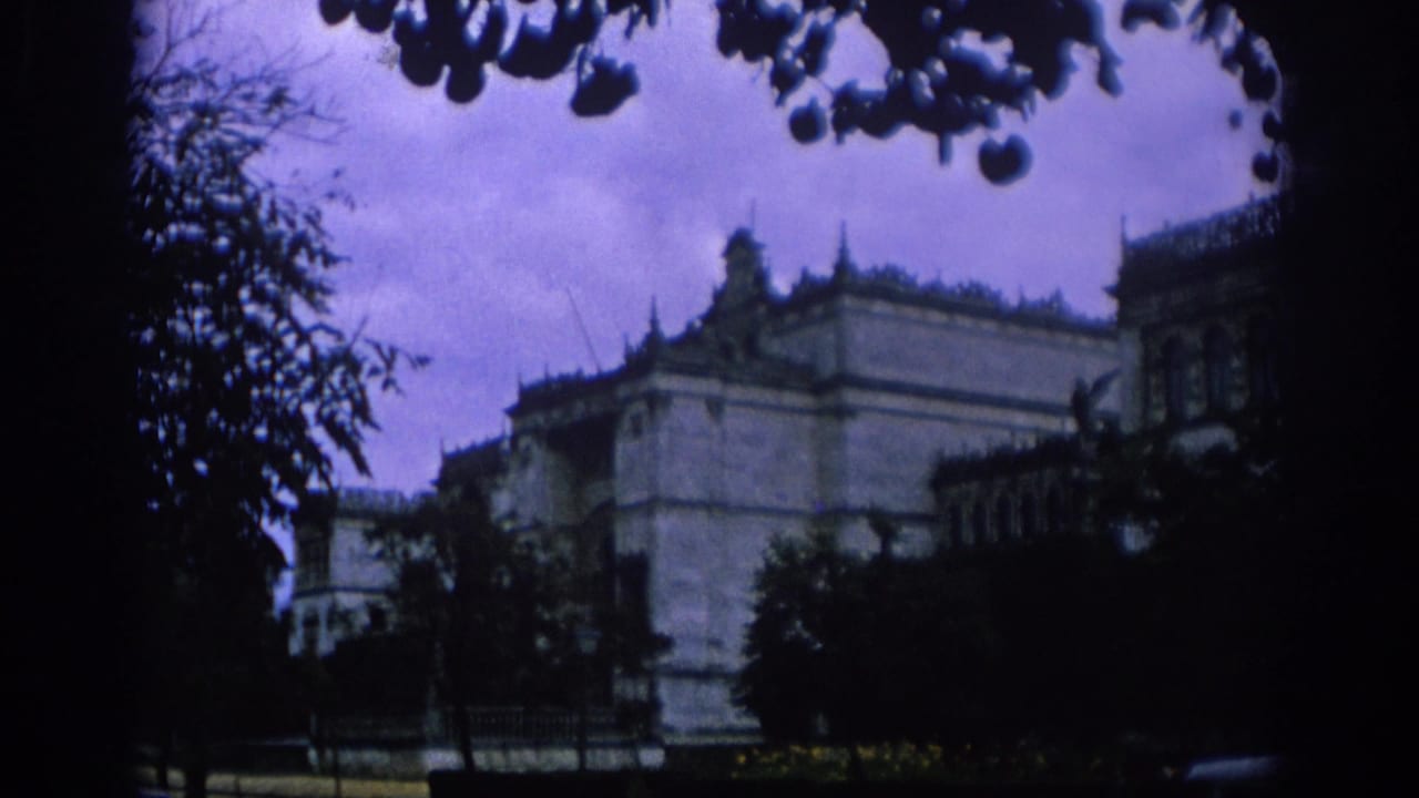1966 Spain travel footage showing a large historic-looking building framed by dark tree branches and a cloudy purple-tinted sky.