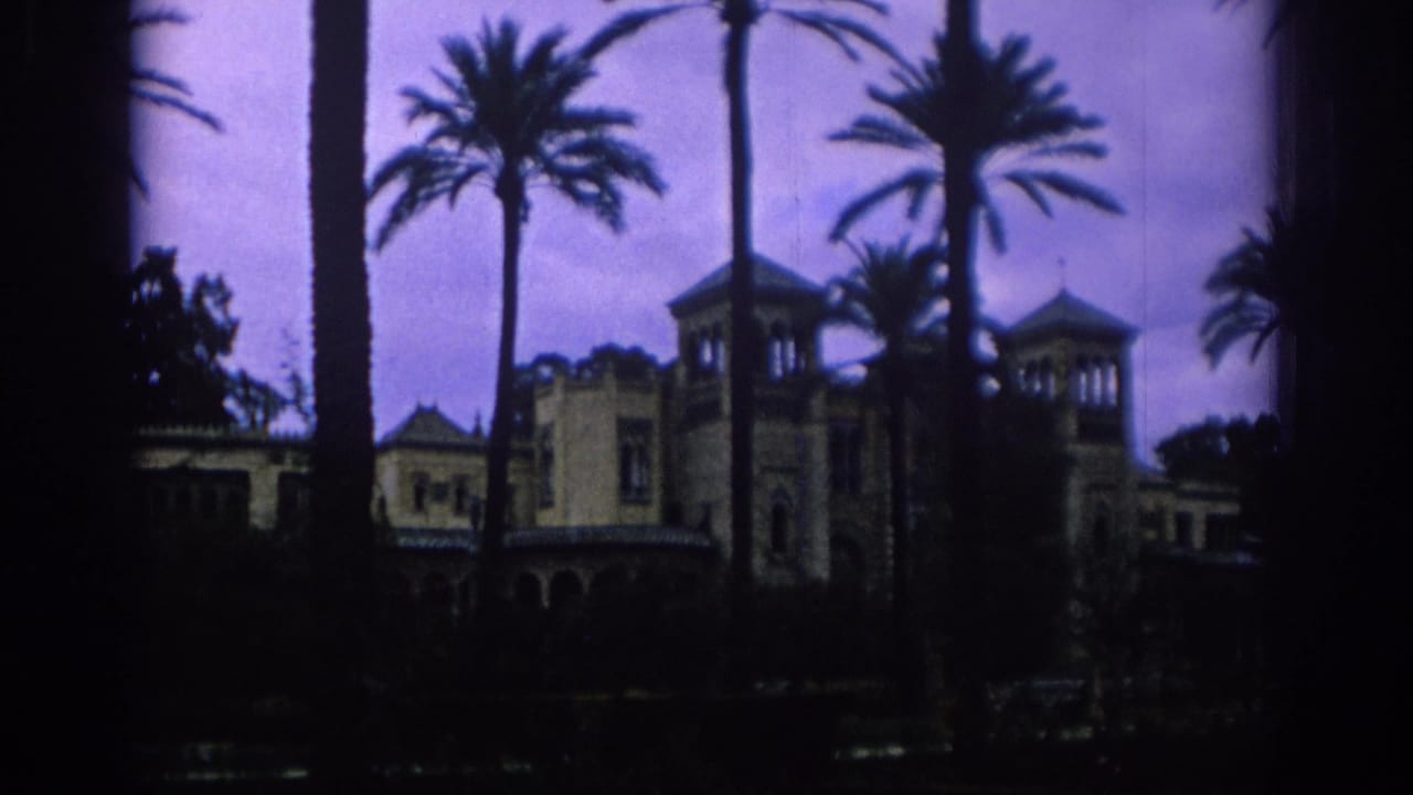 1966 Spain home-movie frame showing a palm-lined resort-like building in soft, dark 8mm color.