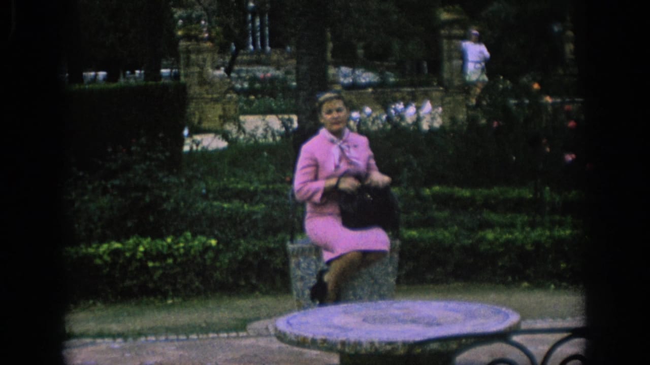 Woman seated in the garden holds or adjusts a dark handbag.